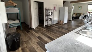 Cocina compacta con un lavamanos, una hornilla y un microondas. Hay un banco de madera y un cubo de basura negro.