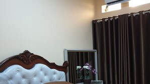 Ein Hotelzimmer mit Bett, Nachttisch mit Lampe, Fenster mit Vorhängen und Klimaanlage.