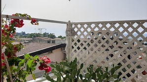 A balcony with a potted plant, a white lattice partition, and a view of the cityscape.