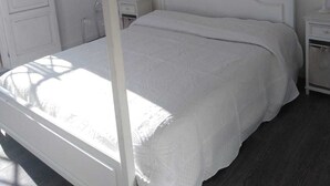 A four-poster bed with a white frame and a beige canopy, a bedside table, and a nightstand.