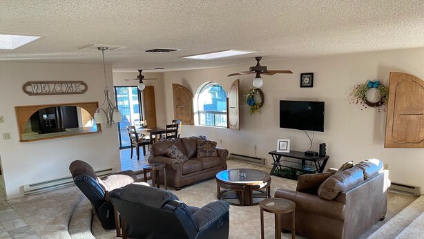 A spacious living room with a large sofa, a coffee table, and a TV. There is a dining area with a table and chairs, and a kitchen area with a microwave and a coffee machine. - Charming home in Country Club Estates (Sierra Vista)