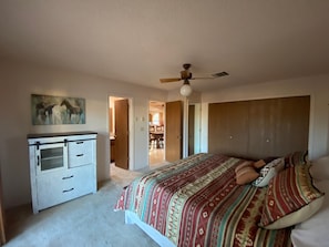 A bedroom with a bed, a dresser, a ceiling fan, and a painting on the wall.