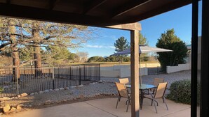 A covered patio area with a table and chairs, a metal fence, and a view of trees and a building in the background. - Charming home in Country Club Estates (Sierra Vista)