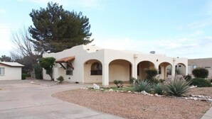 A single-story building with a beige facade, multiple arched windows, and a small patio area with landscaping. - Charming home in Country Club Estates (Sierra Vista)