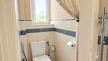 A small bathroom with a toilet, a shower, and a window.