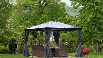 Um gazebo com mesa e cadeiras, cercado por vegetação exuberante e árvores.