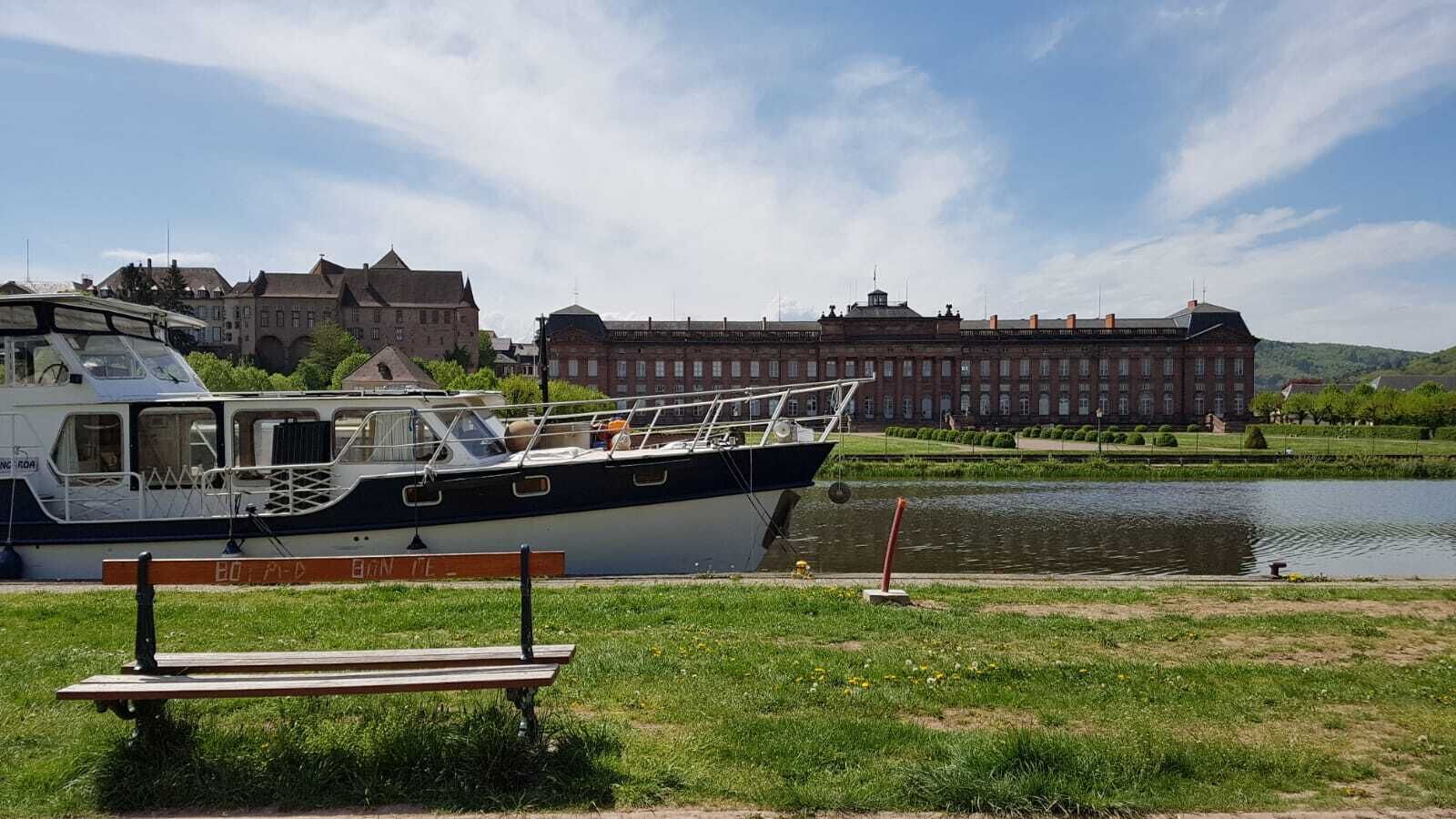 Ein Boot liegt an einem Gebäude mit einer Rasenfläche und einer Bank.