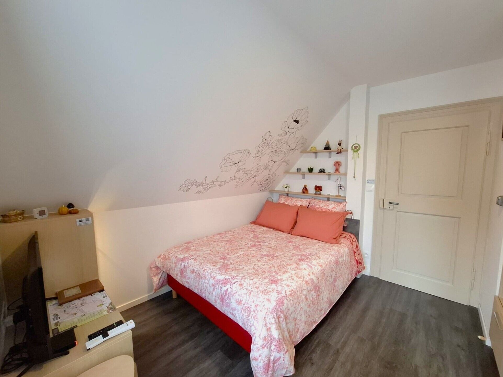 Un dormitorio con cama, cómoda, escritorio con computadora y pared decorada con motivos florales.