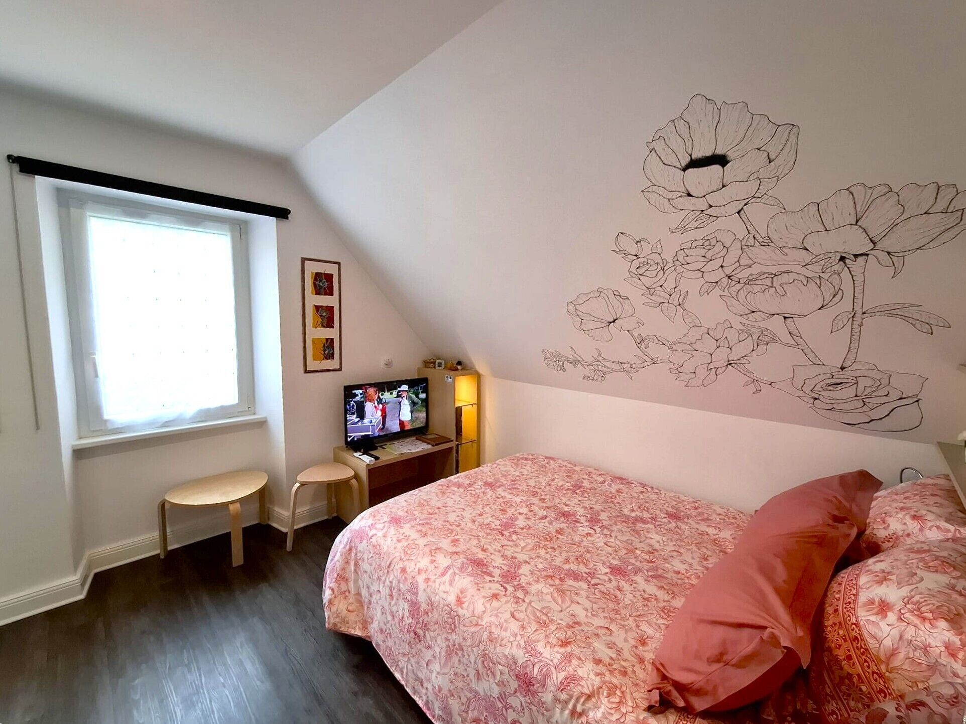 A bedroom with a bed, a TV, a desk, and a window.