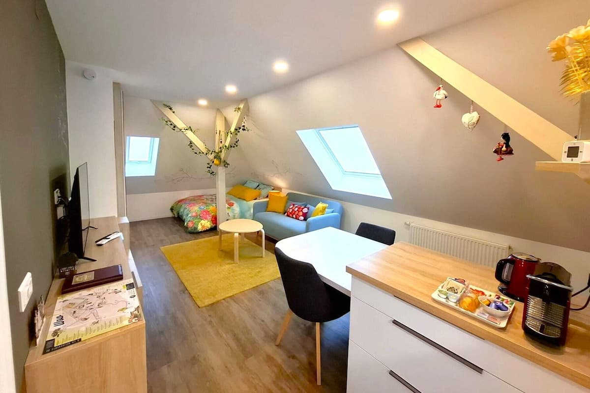 Ein kompakter Wohnbereich mit Essplatz, einer Couch, einem kleinen Tisch und einer Küchenzeile mit Wasserkocher und Kaffeemaschine.