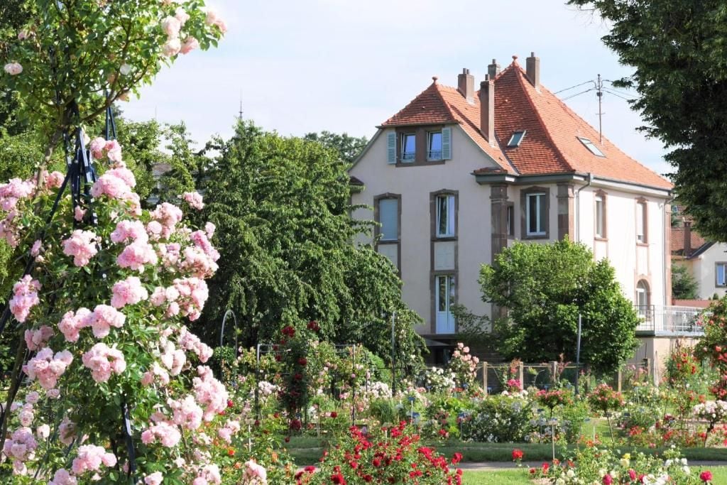 A two-story house with a red-tiled roof, surrounded by a well-maintained garden with various flowering plants.