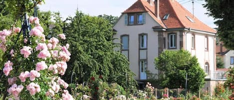 A two-story house with a red-tiled roof, surrounded by a well-maintained garden with various flowering plants.