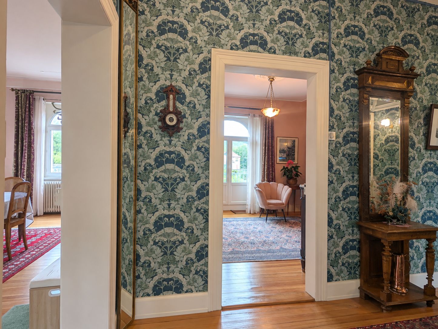 A room with patterned wallpaper, a wooden floor, a mirror, and a chair.