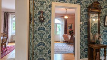 A room with patterned wallpaper, a wooden floor, a mirror, and a chair.