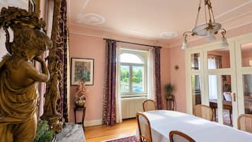 Une salle à manger avec une table en marbre, des chaises en osier, un tapis rouge à motifs et une statue de femme.