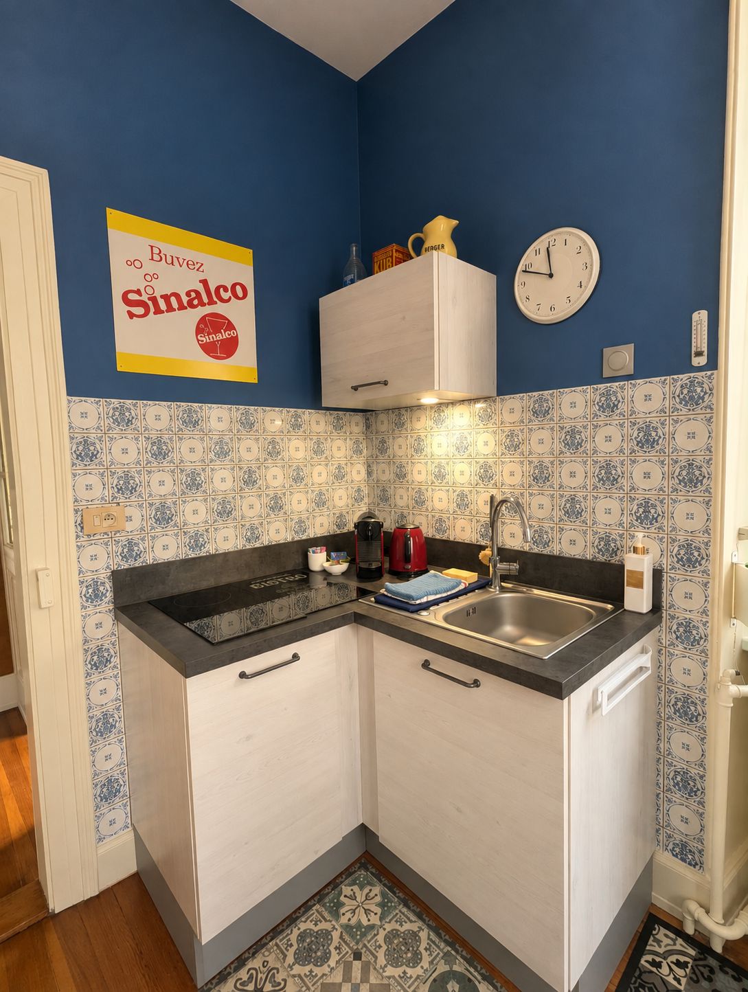A compact kitchen with a sink, stove, and a clock on the wall.