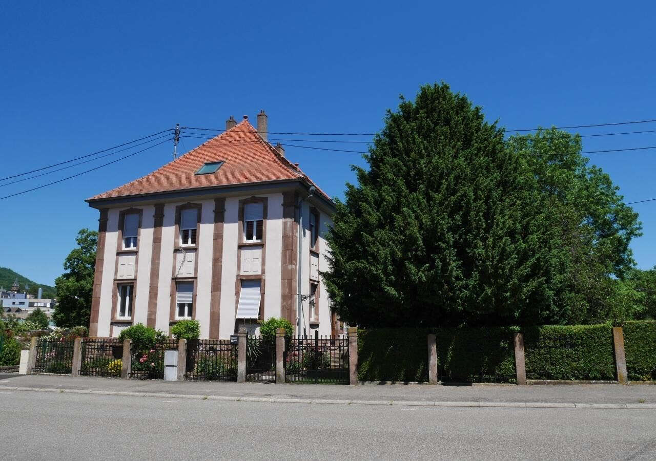 A multi-story building with a red-tiled roof, a gated entrance, and a large tree in front.