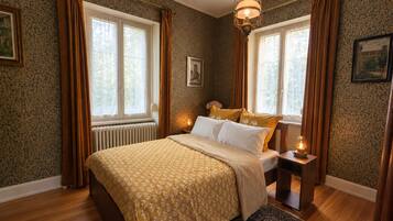 A bedroom with a bed, two bedside tables, a nightstand, a patterned rug, and a window with curtains.