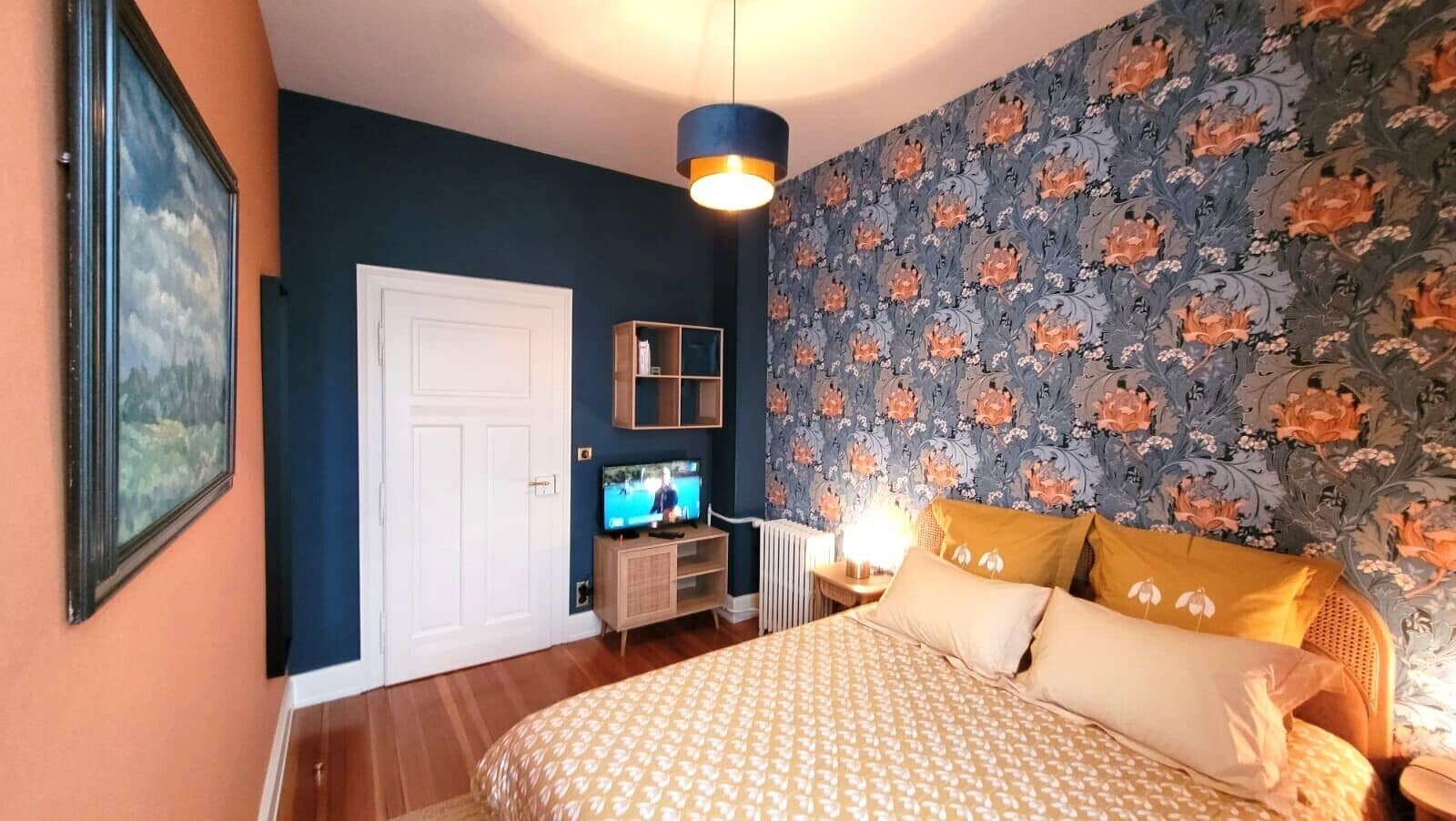 A bedroom with a bed, a television, a dresser, and a wall with floral wallpaper.