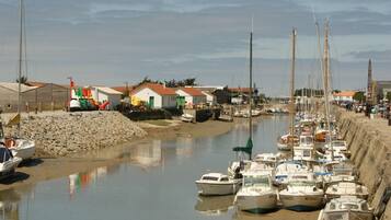 Un port de plaisance où de nombreux bateaux sont amarrés le long de la côte, entouré de petits bâtiments et d’une plage de sable.