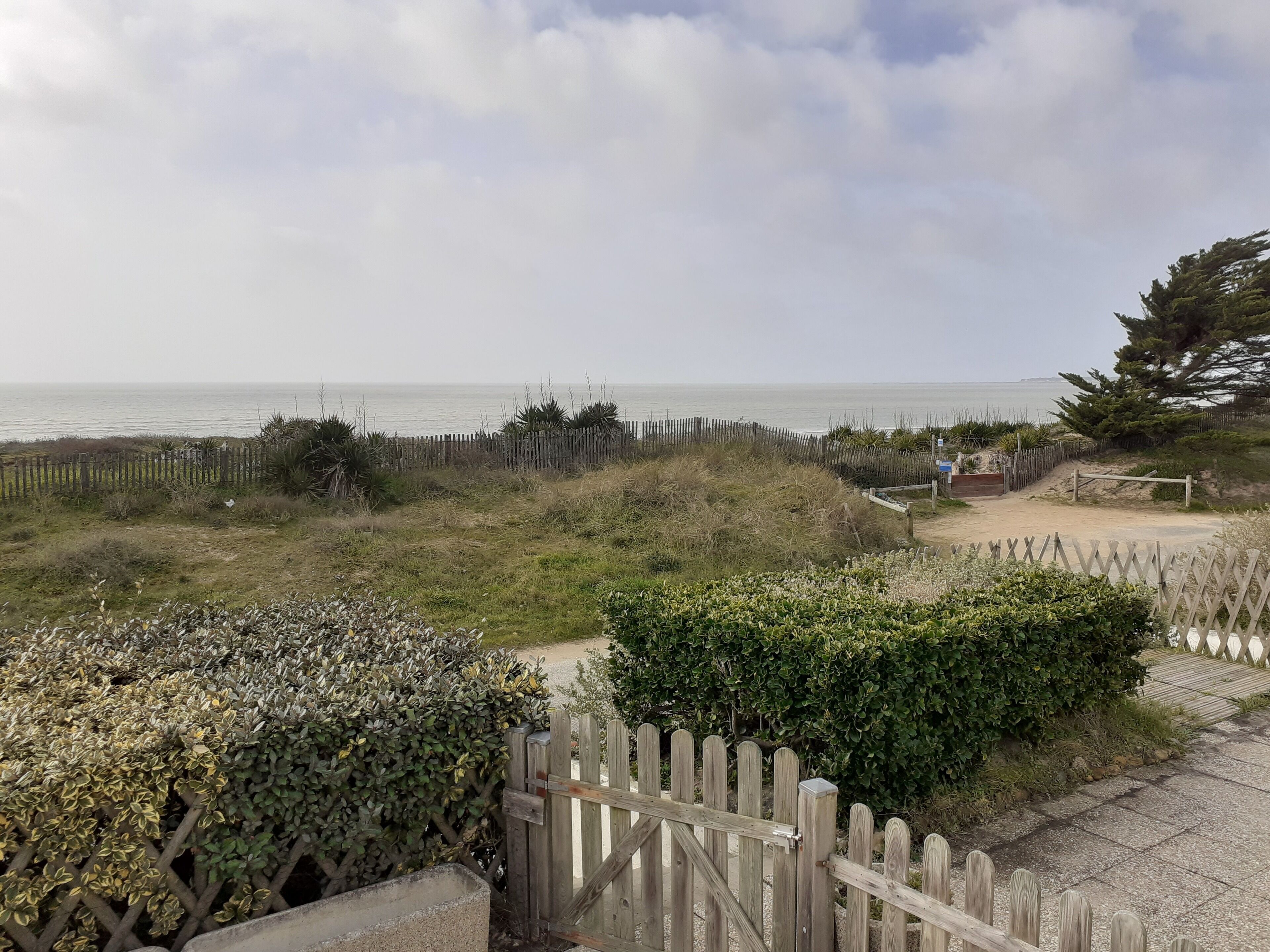 Un sentier côtier menant à une plage, avec une clôture en bois et un panneau indicateur.