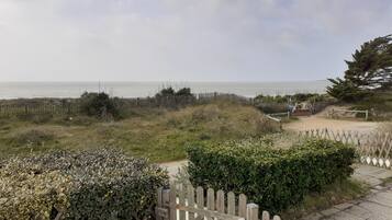 Un sentier côtier menant à une plage, avec une clôture en bois et un panneau indicateur.