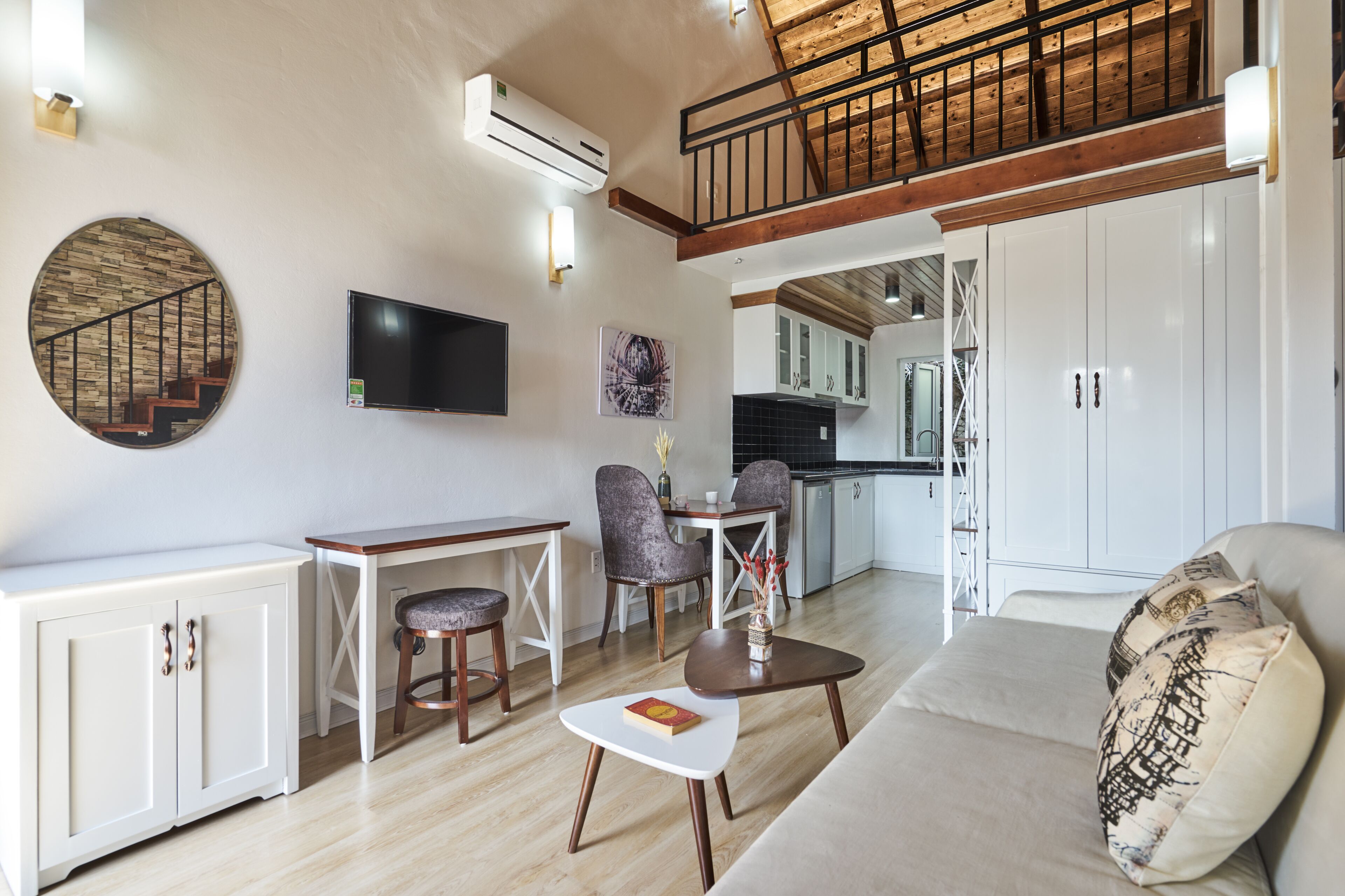 Un salon moderne avec un canapé, une table basse et un téléviseur fixé au mur. On aperçoit un coin cuisine à l’arrière-plan.