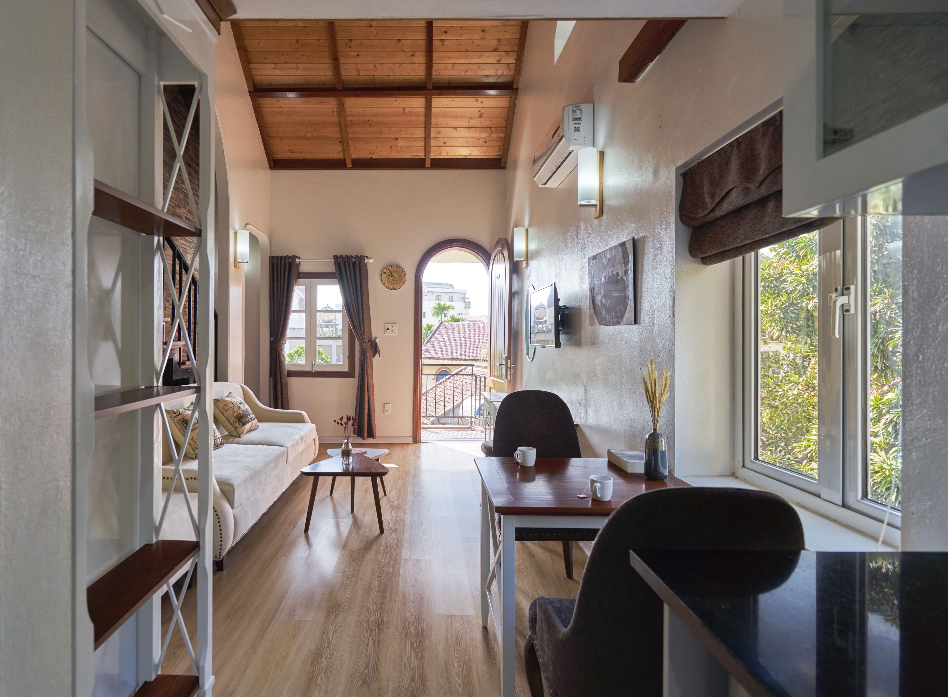 A spacious room with a wooden ceiling, a dining area with a table and chairs, a sofa, and a view through an open door to the outside.