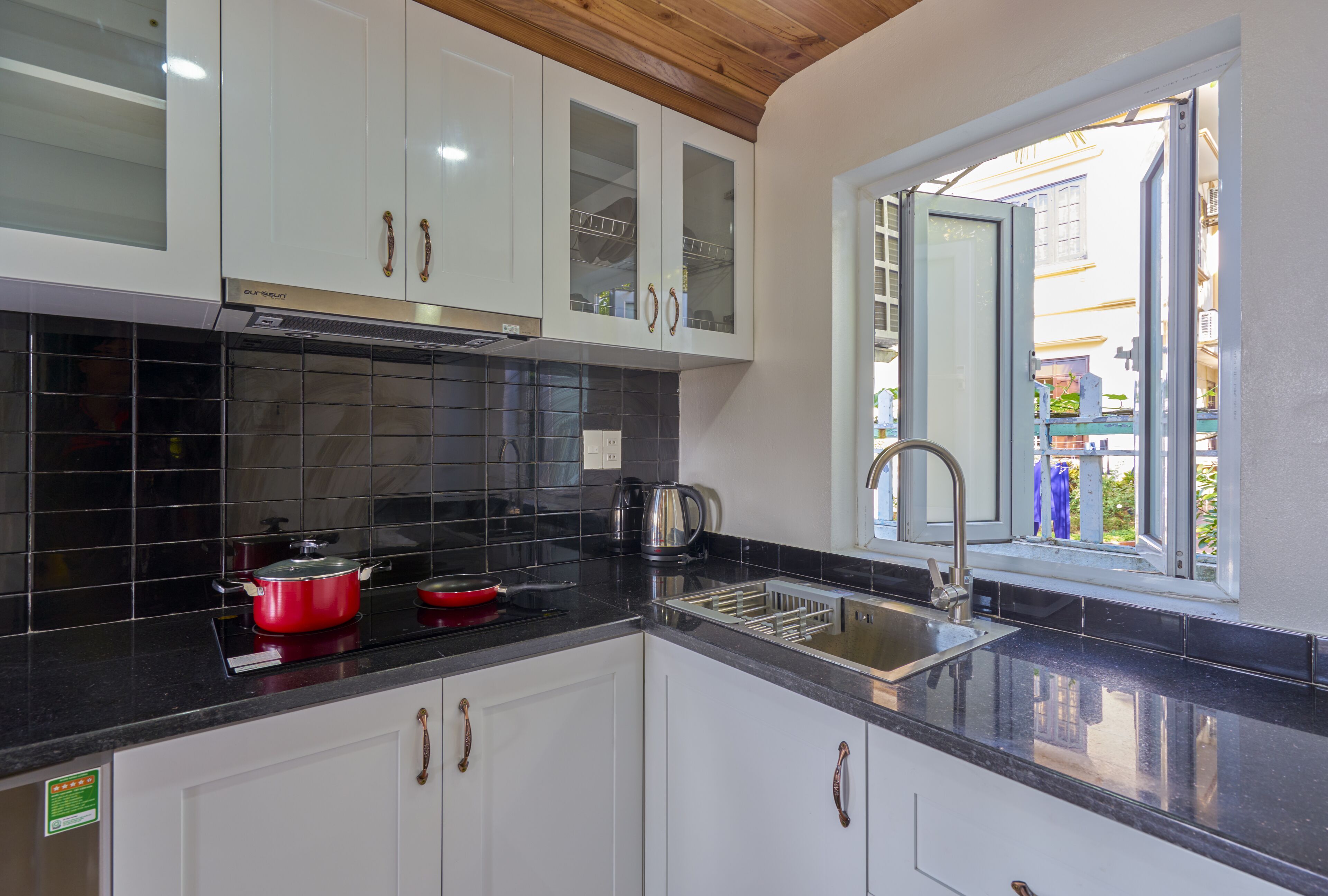A kitchen with white cabinets, a black countertop, a red pot, and a window with a view of the outside.