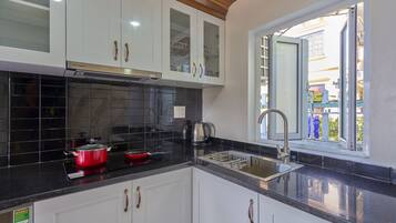 A kitchen with white cabinets, a black countertop, a red pot, and a window with a view of the outside.