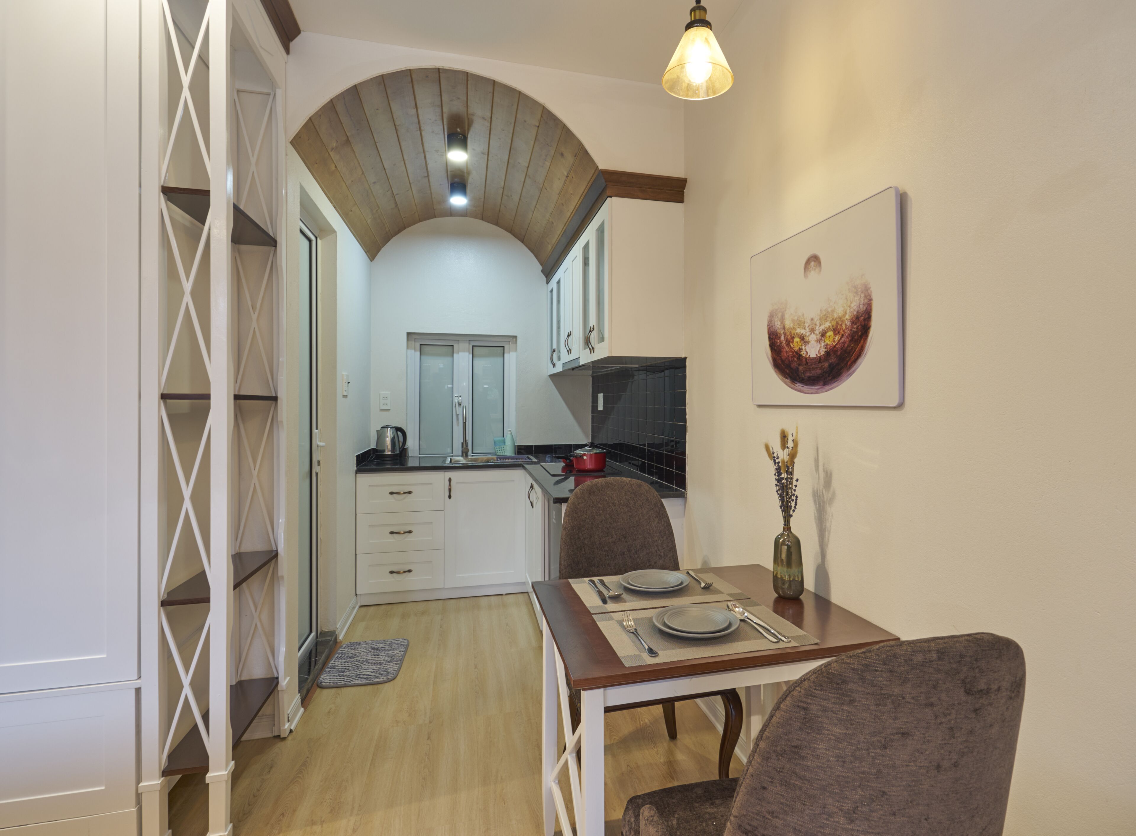 A compact kitchen with white cabinets, a wooden ceiling, and a dining area with a table set for two.