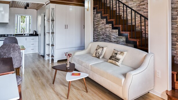 Ein großzügiger Wohnbereich mit hoher Decke, einer Treppe mit Steinwand und einem weißen Sofa mit Zierkissen.