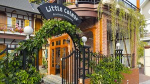 Der Eingang eines Boutique-Hotels mit Backsteinfassade, einer Holzw pergola und einem Schild mit der Aufschrift 'Little Colmar Boutique Homes'.