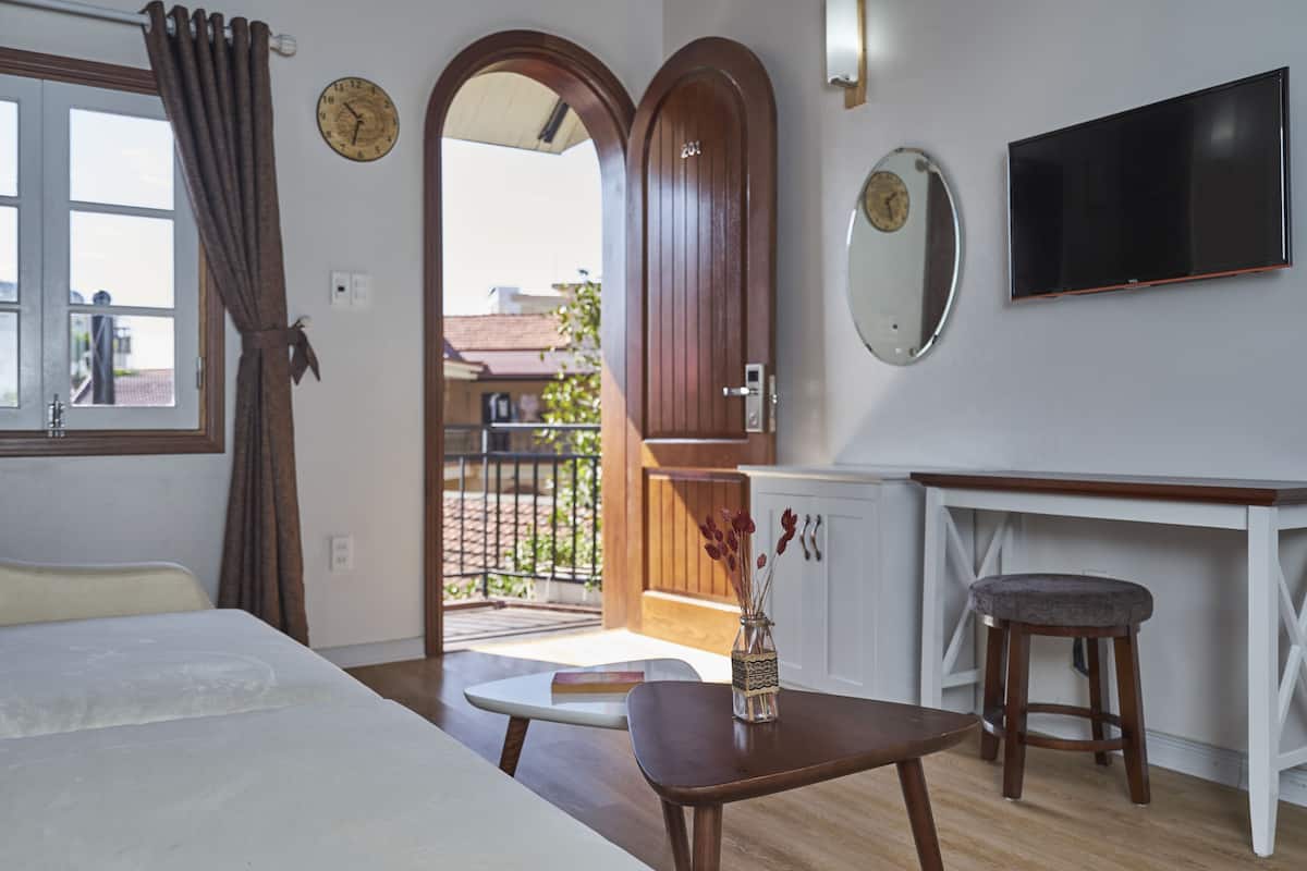 A hotel room with a bed, a small table, a TV, a mirror, and a door leading to an outdoor balcony.