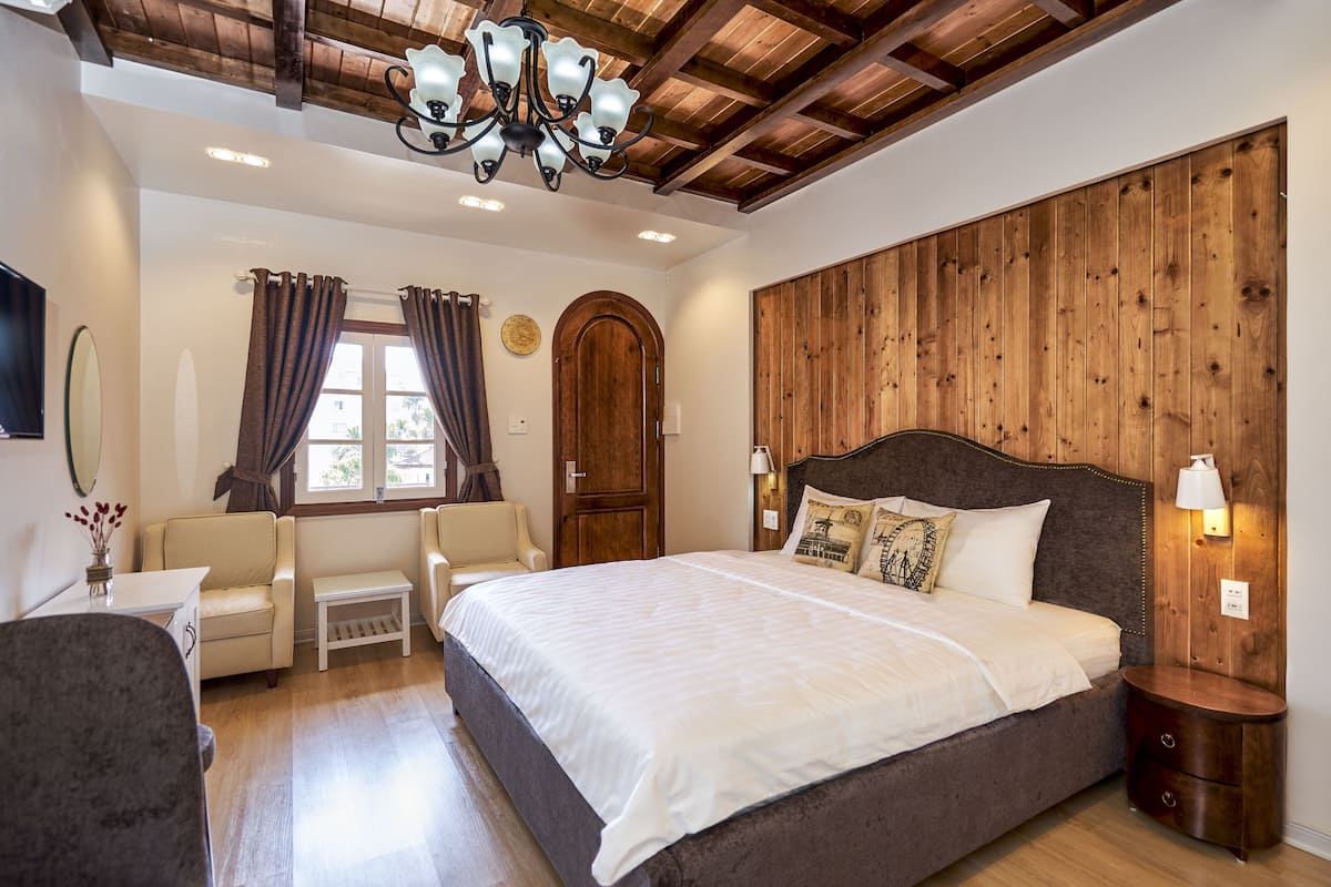 A bedroom with a large bed, wooden paneling on the wall, a chandelier, and a small bedside table with a lamp.