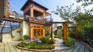 Ein zweistöckiges Gebäude mit Balkon, einer Holzpergola und einem Garten mit Brunnen.