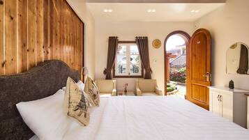 A bedroom with a large bed, wooden paneling, a small table with chairs, and a view of the outside.