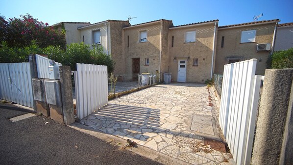 A residential street with houses, a paved driveway, and a white gate.