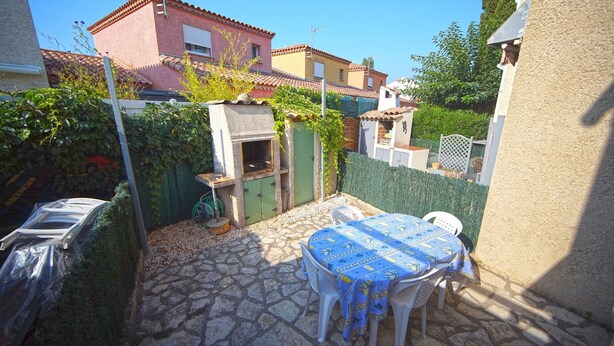 A patio with a stone floor, a table with a blue tablecloth, and a grill area. - House in Grau d'Agde, 300 meters from the sea (Agde)