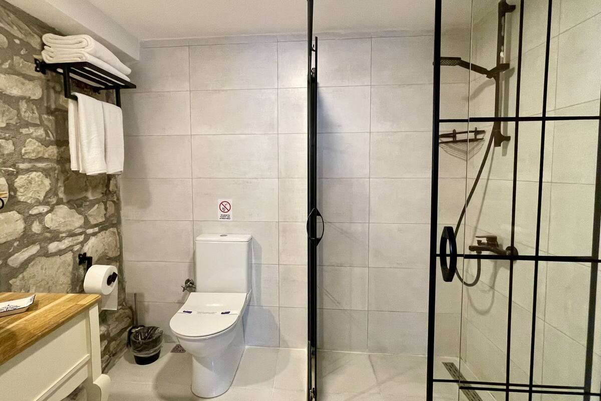 A bathroom with a toilet, a shower, and a towel rack with folded towels.