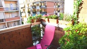 A balcony with a pink chair, potted plants, and a view of adjacent buildings. - Egle's House (Roma)