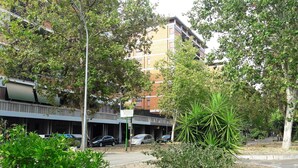 A multi-story building with a parking area and greenery in front. - Egle's House (Roma)
