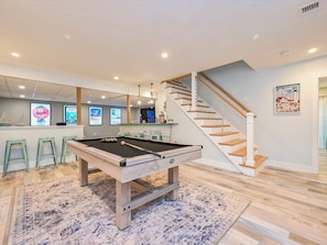 Relax in a spacious room with a pool table, wooden staircase, and large window.