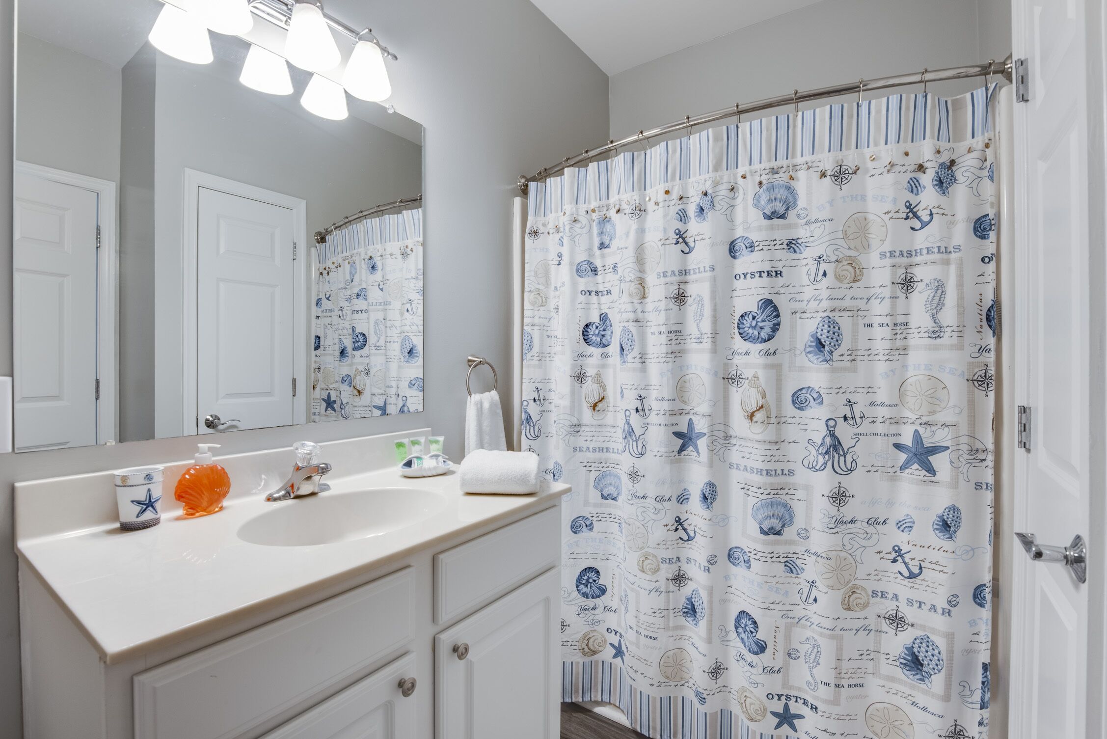 A bathroom with a white sink, a mirror, and a shower curtain with nautical designs.