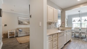 A modern kitchen with white cabinetry, a dining area with a table and chairs, and a living room with a sofa and a painting on the wall. - High Tech Hideaway: The modern beach lifestyle (Rehoboth Beach)