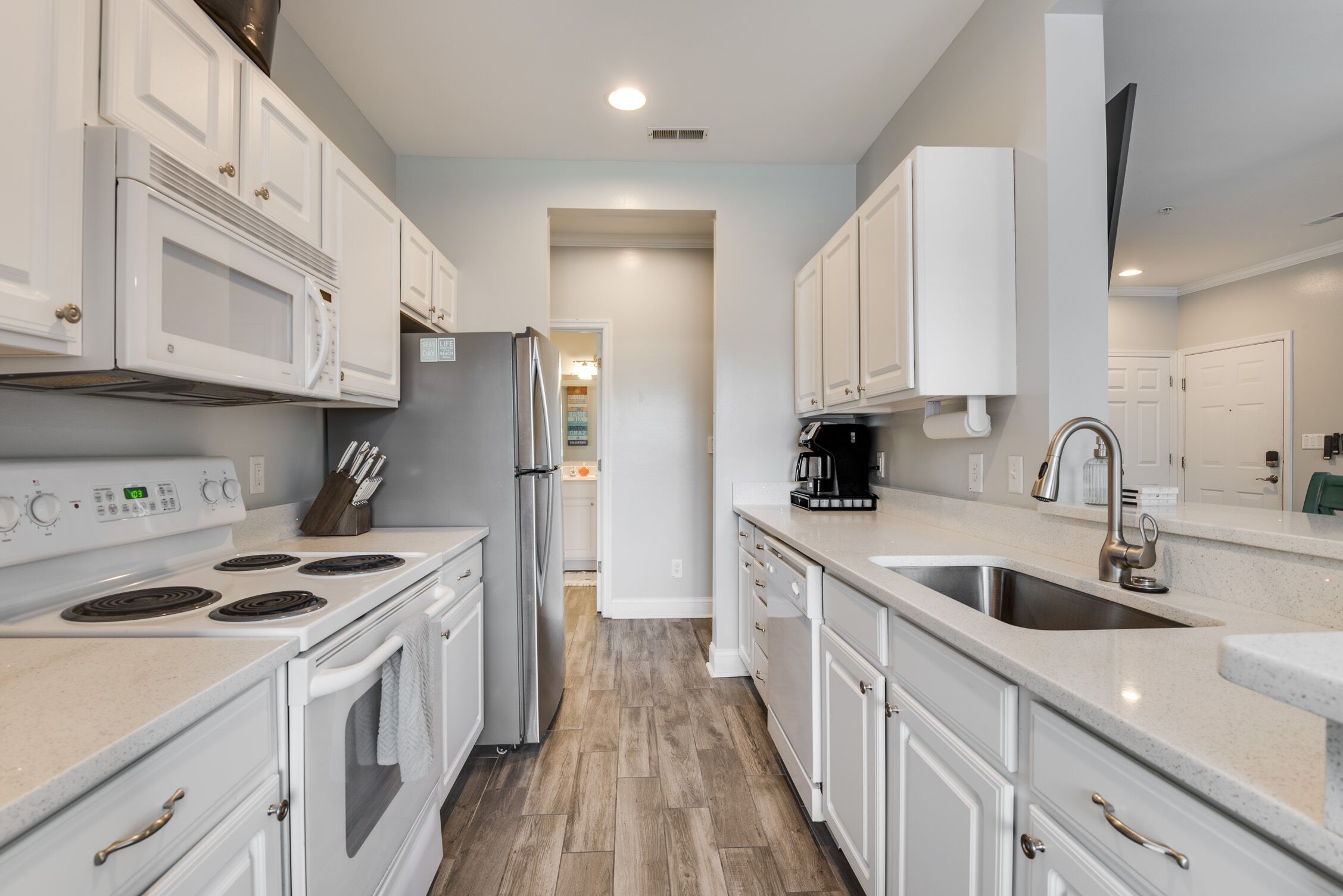 A modern kitchen with white cabinets, a stainless steel refrigerator, a built-in microwave, a stove, and a sink.