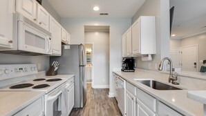 A modern kitchen with white cabinets, a stainless steel refrigerator, a built-in microwave, a stove, and a sink. - High Tech Hideaway: The modern beach lifestyle (Rehoboth Beach)