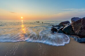 A beach with rocks and waves at sunset.