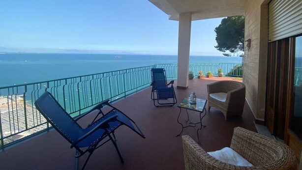Ein Balkon mit Meerblick, zwei Liegestühle, ein kleiner Tisch und ein Korbstuhl.