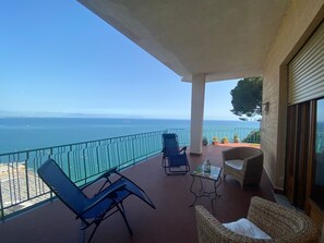 A balcony with a view of the sea, two lounge chairs, a small table, and a wicker chair.